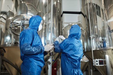 Kimya fabrikasında üretim sırasında koruyucu giysiler giyen iki işçinin arka planı.