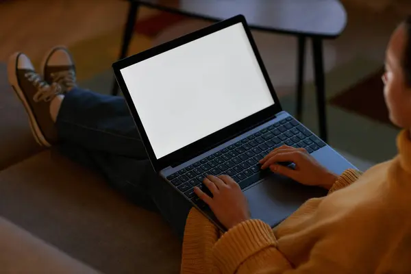 Side view of young woman using laptop with white screen in cozy home setting, copy space