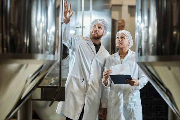 食品工場で装置を点検する実験室のコートを身に着けている2人の労働者の肖像画を待って下さい — ストック写真