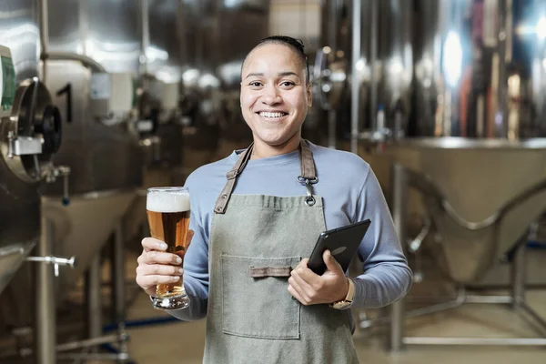 ビールグラスを持っている笑顔の女性の肖像画をウエストし 醸造工場で働いている間カメラを見ます — ストック写真
