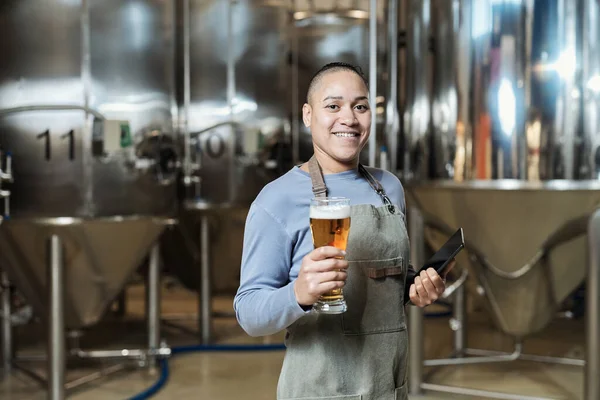 ビールグラスを保持し 醸造工場で働いている間カメラを見ている笑顔の女性醸造所の肖像画を待って下さい — ストック写真