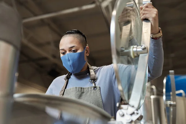 ビール製造工場でマスク開口タンクを着用した女性ブリューマスターの低角度の肖像画 — ストック写真