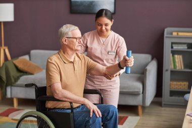 Sosyal hizmet görevlisi rehabilitasyonu sırasında engelli bir adama yardım ediyor. Kollarını dambıllarla eğitiyor.