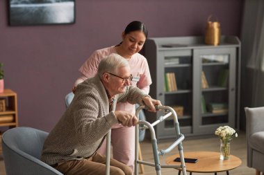 Rehabilitasyonu sırasında erkekleri önemseyen genç sosyal hizmetler uzmanı Walker 'ın yanında ayağa kalkmasına yardım ediyor.