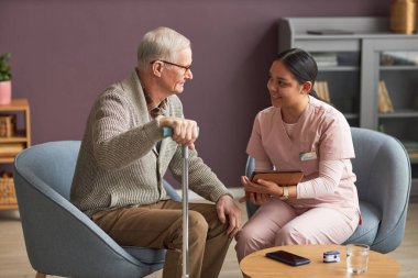 Onlar oturma odasındaki koltuklarda otururken kıdemli adam sosyal hizmet görevlisiyle konuşuyor.