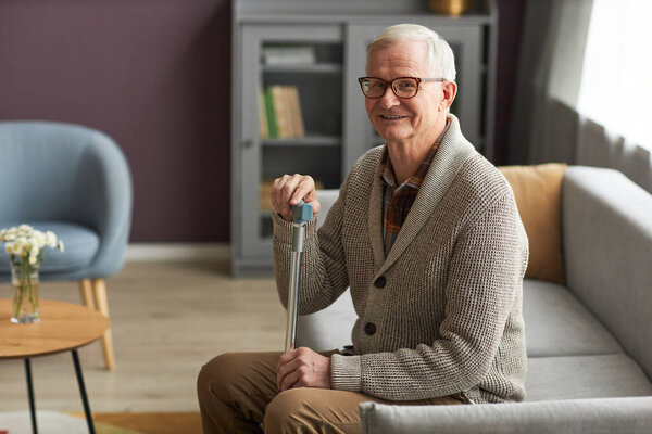 Portrait of elderly man smiling at camera while resting on sofa in the living room