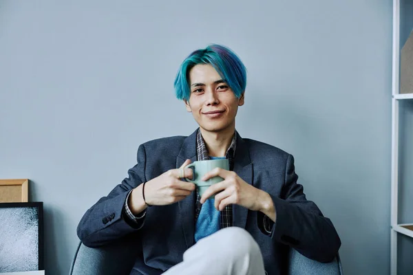 Minimal front view portrait of Asian young man with colored blue hair smiling at camera and holding mug