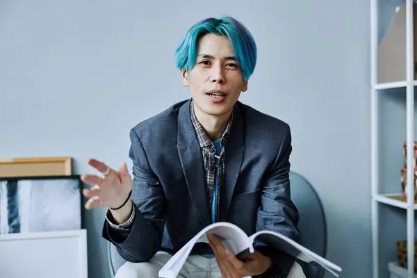 Minimal portrait of Asian young man with colored blue hair talking and looking at camera in office