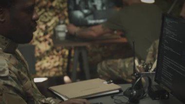 Odaklanmış Afrikalı Amerikalı erkek ordu subayının belini kaldırın. Kamuflaj üniforma programı, bilgisayardan kodlanıyor. Geceleri iş arkadaşlarıyla birlikte çalışırken.