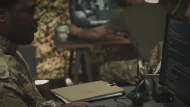 夜間にオフィスで同僚と作業しながら コンピュータ上でプログラムをコーディングするカモフラージュに焦点を当てたアフリカ系アメリカ人男性軍士官のウエスト — ストック動画