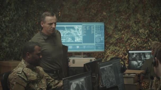 身着迷彩服的不同族裔军事监视人员在夜间合作 用雷达和闭路电视摄像机观看电脑屏幕的中景照片 — 图库视频影像