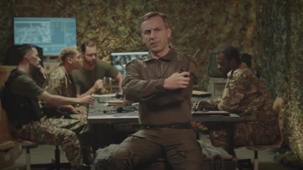 真剣な白人男性軍事コントロールセンター司令官のミディアム肖像画 ウォルキー トーキーが椅子に座ってカメラを見ながらバックグラウンドで働いている — ストック動画