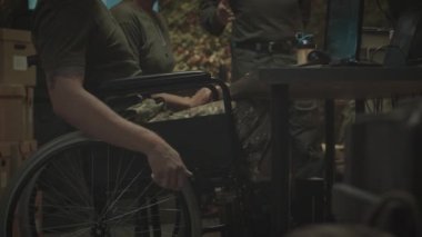 Tekerlekli sandalyedeki beyaz erkek askerin bilgisayardaki izleme programıyla çalışma masasına yaklaşırken ve askeri kontrol bürosunda çalışırken görüntülerini yukarı doğru eğ.