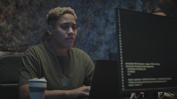 同僚と夜のダークオフィスに座っているラップトップコンピュータのプログラムコードを入力するBiracial女性の軍事サイバーセキュリティワーカーのウエスト — ストック動画