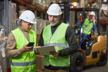 Depoda pano tutan ve yansıtıcı ceketler giyen iki işçinin belini kaldırın.