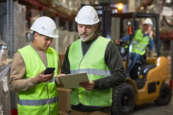 Depoda pano tutan ve yansıtıcı ceketler giyen iki işçinin belini kaldırın.