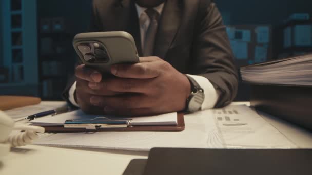 非洲裔美国商人坐在写字台前 午夜工作时 在智能手机上输入信息 并在笔记本上记笔记 这让人难以辨认 — 图库视频影像