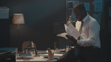 Siyahi girişimcinin gece geç saatlere kadar ofiste çalışırken masa başına eğilip evrak işleriyle uğraşırken ve paket erişte yerken orta boy bir fotoğrafı.
