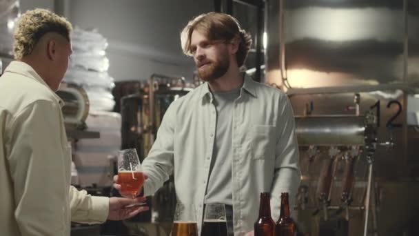 醸造所で排気を行っている白人男性ビール専門家のミディアムショットは 試してみるために訪問者に新鮮なラガーのガラスを与えます — ストック動画
