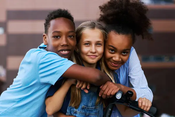 2人のアフリカ系アメリカ人の子供が電動スクーターと彼らのコーカサス人の友人を抱擁しながら一緒に時間を過ごし カメラを見ている — ストック写真