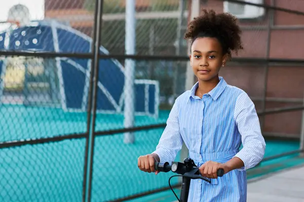 漂亮的非洲裔美国少女 带着电动车 站在运动场边 用体育设施看着摄像机 — 图库照片