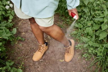 Doğada seyahat ederken bacakları böcek kovucuyla kısırlaştıran siyah kadının yüksek açılı yakın çekimi.