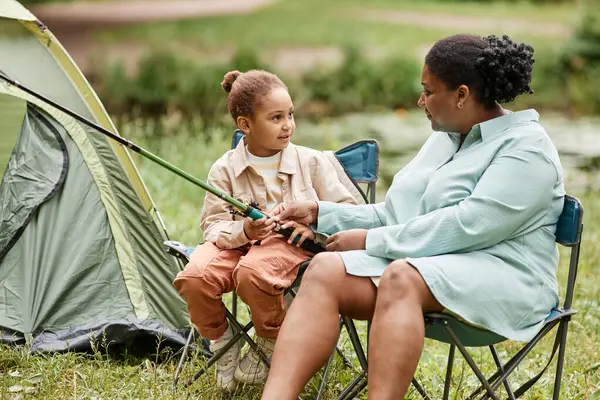 Portrait of black mother and daughter camping together outdoors and holding fishing rod