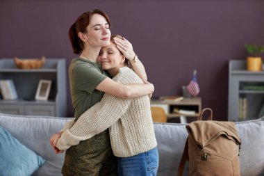 Evinde kızını kucaklayan genç bir askerin samimi portresi.