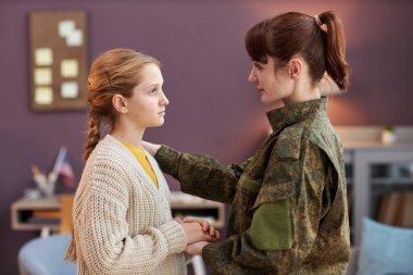 Evde kızıyla el ele tutuşan asker annenin yan görünümü.