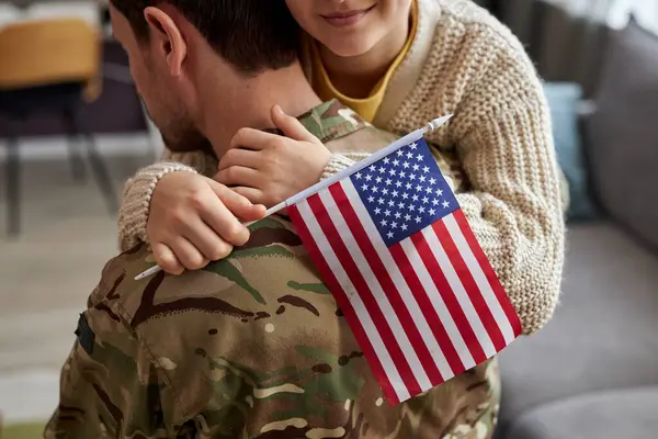 Candid close up of girl embracing military dad and holding american flag, copy space
