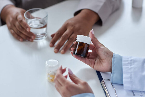 Close up of female doctor holding bottle of pills and explaining medication to patient in clinic