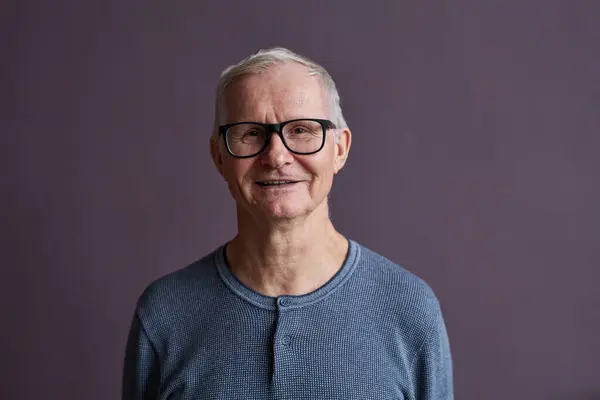 Minimal portrait ot of senior man wearing glasses and smiling at camera against purple background, copy space