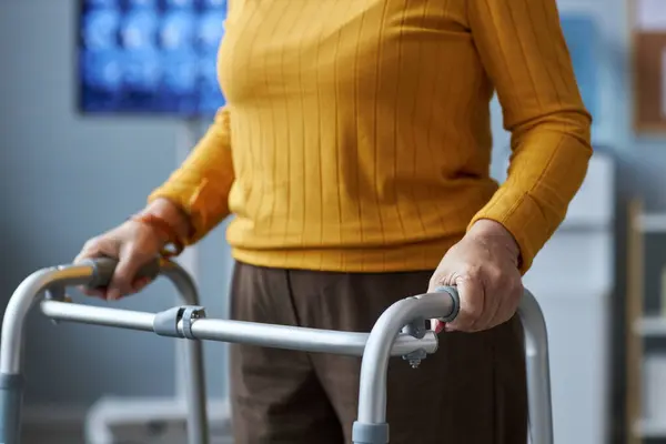 Close up of senior woman using mobility walker in medical clinic setting, copy space