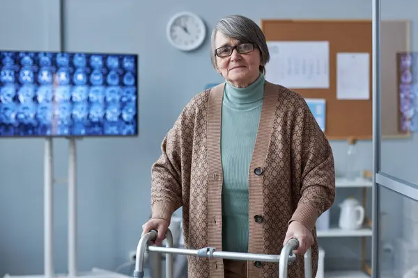 Waist up portrait of grey haired senior woman using mobility walker in medical clinic, copy space