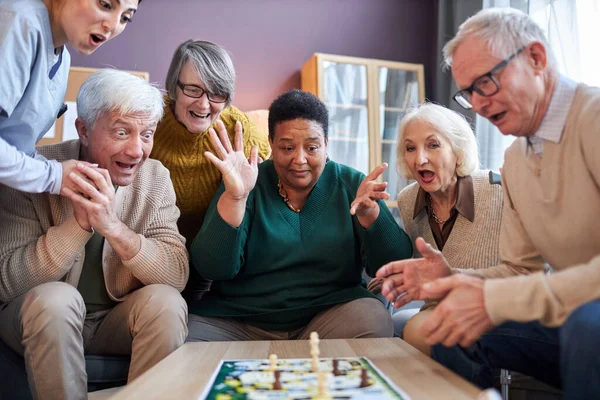 Multiethnic group of senior people playing board games at retirement home with surprised emotion