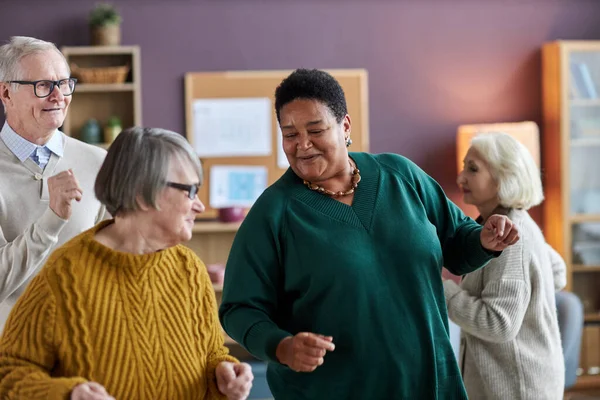 Waist up portrait of black senior woman dancing with friends in retirement home and smiling joyfully