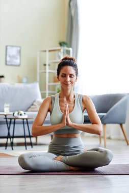 Gülümseyen genç bir kadının dikey portresi. Nilüfer pozisyonunda otururken gözleri kapalı meditasyon yapıyor.