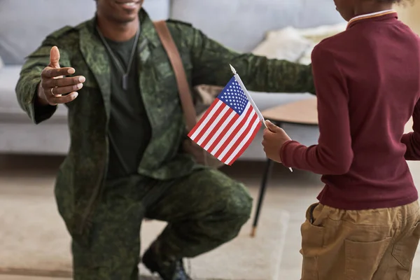Close-up of little girl with american flag meeting her military dad at home, he coming back from war service