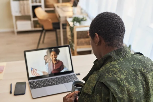 Rear view of military dad talking to his family online on laptop during his war service
