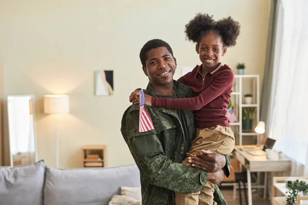 Portrait of military dad with his little daughter smiling at camera standing in the room at home