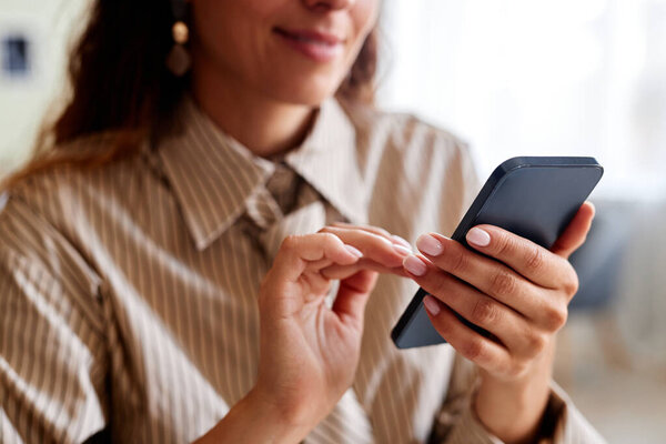 Close up of smiling young woman holding smartphone and tapping screen, copy space