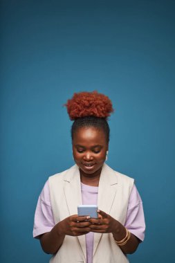 Genç siyahi bir kadının canlı mavi arkaplan üzerinde fotokopi alanı olan akıllı telefon kullanarak minimal portresi