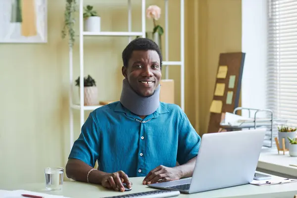 照片上的黑人年轻人 头颈托架 在办公室的办公桌前工作 对着相机微笑 — 图库照片