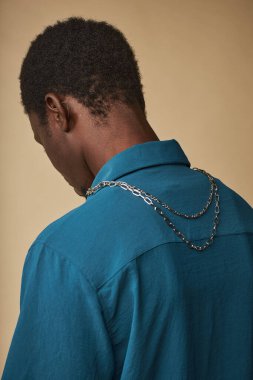 Boyunda metal zincir, moda aksesuarlarıyla kameradan uzak duran genç siyahi adamın dikey arka görüntüsü