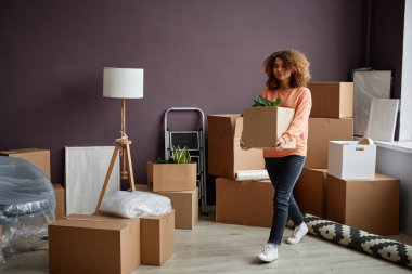 Yeni dairesinde karton kutular taşıyan genç bir kadın.