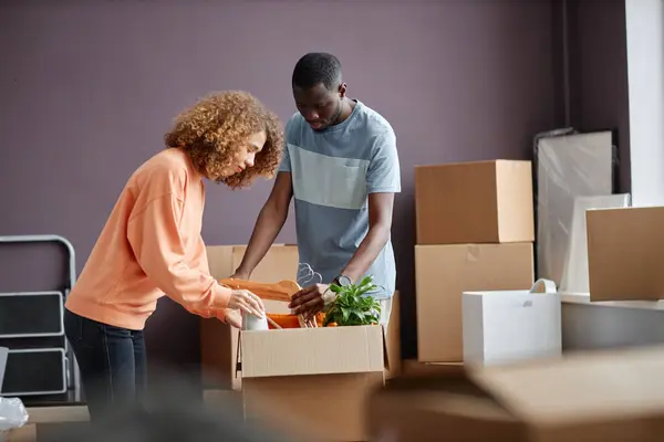 Young multiethnic couple packing things in cardboard boxes for moving to new house