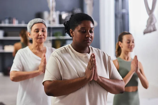 Group of women standing with their eyes closed and doing yoga in health club
