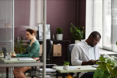Açık ofislerdeki masalarda çalışan iki kişinin portresi canlı yeşil bitkilerle süslenmiş.