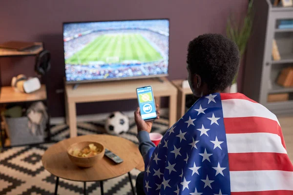 身穿美国国旗的体育迷在家里观看足球比赛的背景图 并使用在线投注应用程序 复制空间 — 图库照片