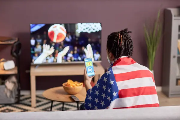 身穿美国国旗的体育迷在家里观看篮球比赛的背景图 并使用在线投注应用程序 复制空间 — 图库照片